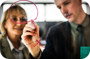 Twee collega’s die een strategie plannen en diagrammen tekenen op een glazen bord.